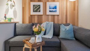 Una sala de estar moderna con un sofá gris, una mesita de madera con un florero, y dos cuadros en la pared.