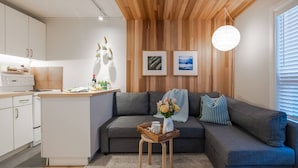 Un espacio habitable moderno con cocina, sofá gris, techo de madera y una obra de arte en la pared.