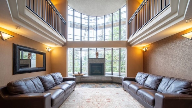 A spacious living room with two leather sofas, a large rug, a fireplace, and a high ceiling with skylights. - Ski-in/Ski-out | Pool & Hot Tub | Sleeps 5! (Whistler)