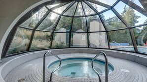 An indoor swimming pool with a glass dome ceiling, surrounded by a tiled floor and metal pool ladders. - Ski-in/Ski-out | Pool & Hot Tub | Sleeps 5! (Whistler)
