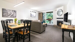 Un salon moderne comprenant un coin repas, une cheminée et une grande fenêtre donnant sur un paysage verdoyant.