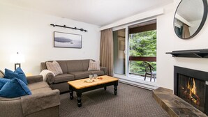 Un salon comprenant un canapé, une table basse, une cheminée et une grande fenêtre donnant sur un paysage verdoyant.