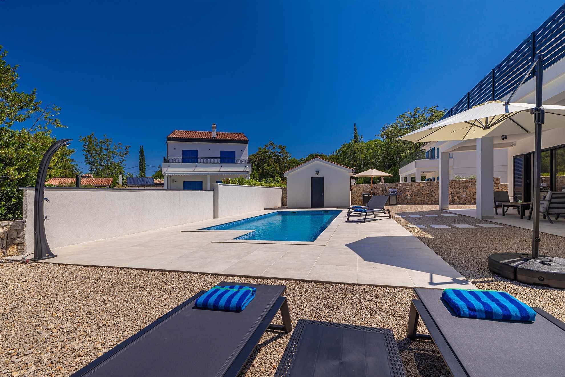 A pool area with two lounge chairs, a small building, and a covered patio.