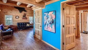 Interieur van een blokhut met een blauwe accentmuur, houten vloeren, een opgehangen dierenkop, een bank en een schilderij.