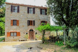 A stone building with a central door, multiple windows with shutters, and a garden area with outdoor furniture. - Podere tra gli Ulivi - Nature, Silence and Yoga (Parrano)