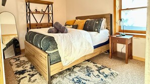 A bedroom with a wooden bed, a bedside table, a mirror, and a window with a view. - Peaceful 2-bedroom apartment - dogs welcome (Granby)
