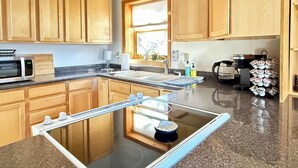 A kitchen with wooden cabinets, a microwave, a coffee maker, and a glass-top island with a sink. - Peaceful 2-bedroom apartment - dogs welcome (Granby)