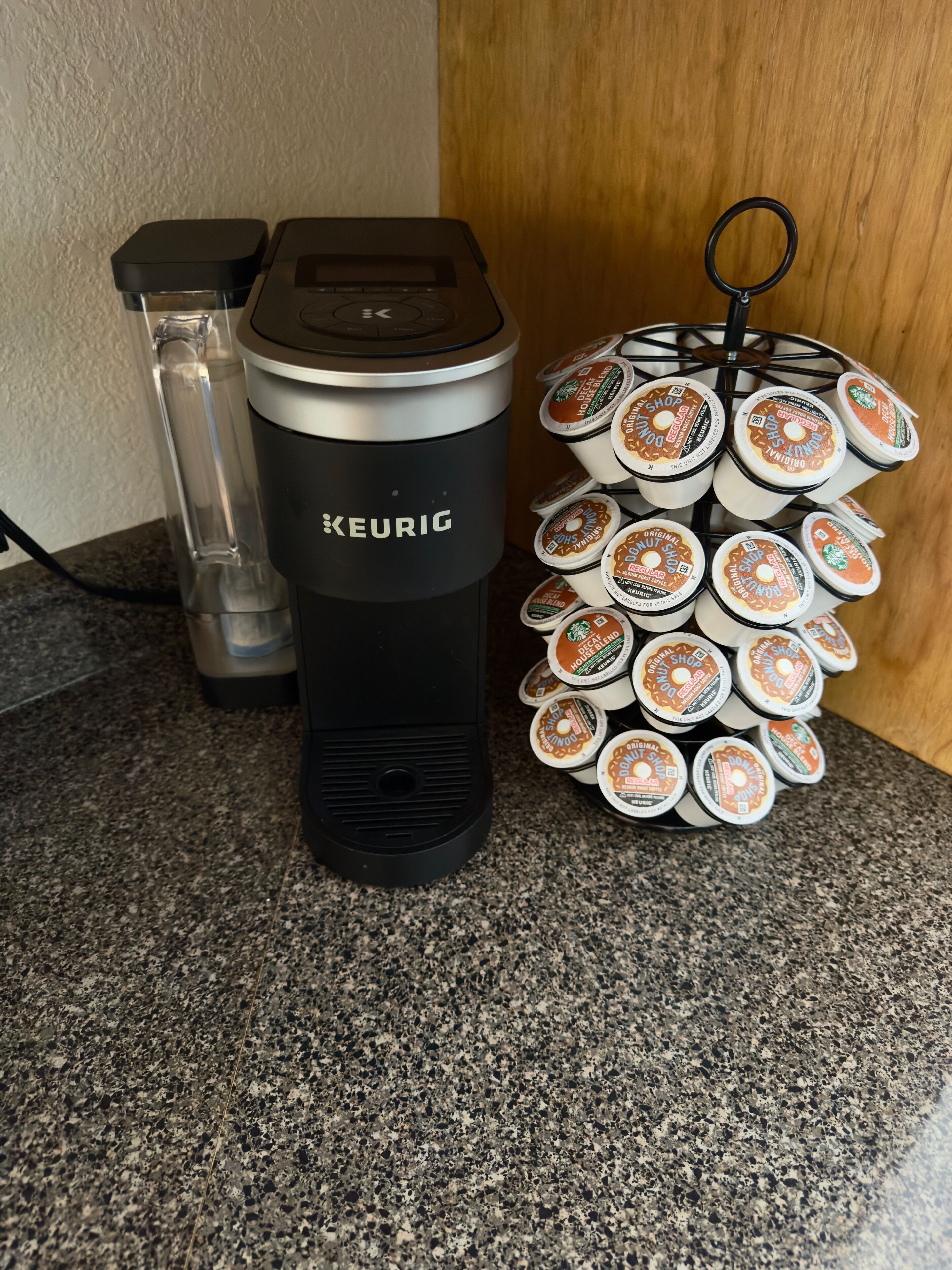 Eine Kaffeemaschine von Keurig und ein Halter für Tassen mit mehreren Kapseln für Keurig auf einer Arbeitsplatte aus Granit.