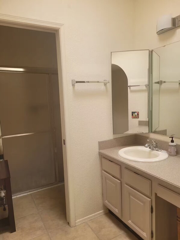 A bathroom with a sink, mirror, towel rack, and a shower door.