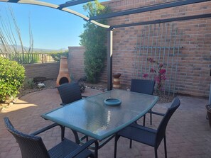 An outdoor patio with a glass table, wicker chairs, a brick wall, and a metal fence. - Beautiful view of Santa Rita Mountains! (Green Valley)