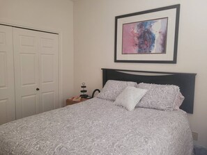 A bedroom with a bed, a nightstand, a framed abstract painting, and a white door. - Beautiful view of Santa Rita Mountains! (Green Valley)