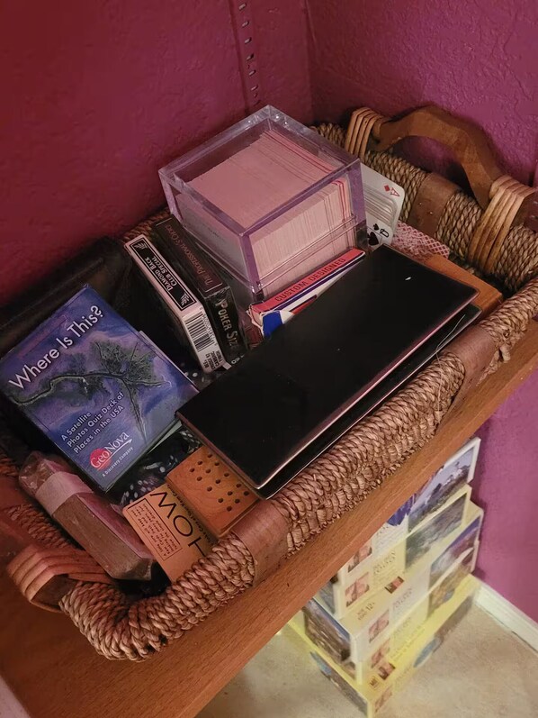 A wooden shelf with a woven basket containing books, a tablet, and a deck of playing cards.