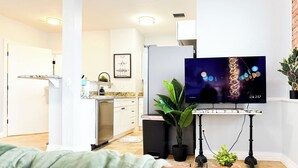 Moderni olohuone, jossa on litteänäyttöinen televisio, sohvapöytä, sohva ja taustalla näkyvä keittiö.