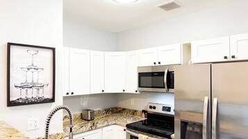 A kitchen with white cabinets, a stainless steel refrigerator, a microwave, a stove, and a water dispenser.