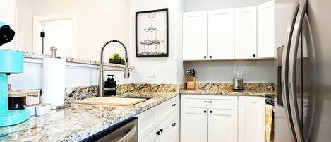 A modern kitchen with white cabinets, a stainless steel refrigerator, a dishwasher, and a granite countertop.