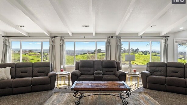 Amplia sala de estar con un gran ventanal que ofrece vistas a un paisaje verde, dos sofás, una mesa de centro y una lámpara en una mesita auxiliar.