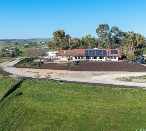 Un edificio con techo rojo y paneles solares, rodeado de vegetación y un sendero de tierra.