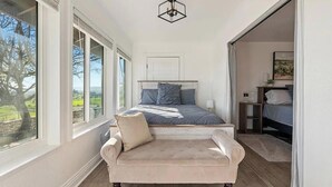 Un dormitorio con cama, una silla, una mesita de noche y ventana con vistas al verdor.