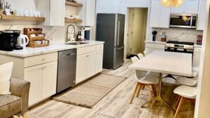A modern kitchen with white cabinetry, a built-in oven, and a dining area with a white table and chairs.