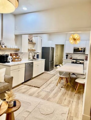 Cozinha moderna com armários brancos, forno embutido e área de refeições com mesa e cadeiras brancas.