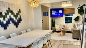 A modern meeting room with a long table and white chairs, a television, and a decorative wall hanging.