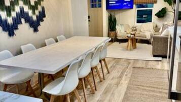 Une salle de réunion moderne, dotée d’une longue table et de chaises blanches, d’un téléviseur et d’une décoration murale.