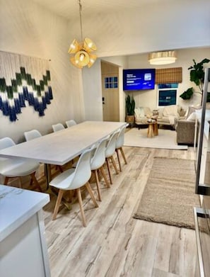 Uma sala de reuniões moderna com uma mesa comprida e cadeiras brancas, uma televisão e um painel decorativo na parede.