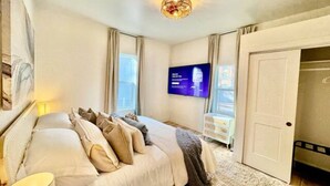 A bedroom with a bed, a TV mounted on the wall, and a door leading to another room.