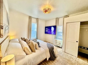 Quarto com cama, televisão na parede e porta para outro cômodo.