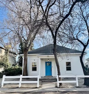 Uma casa branca com porta azul, cercada por árvores sem folhas e um cercado branco.