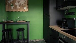 A kitchen with a green wall, a wooden world map, a coffee machine, and two black stools. - Jungle Suite with Spa Bath – Exotic Getaway in Le Havre (Le Havre)