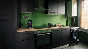 A compact kitchen with black cabinets, a built-in oven, a coffee maker, and a washing machine. - Jungle Suite with Spa Bath – Exotic Getaway in Le Havre (Le Havre)