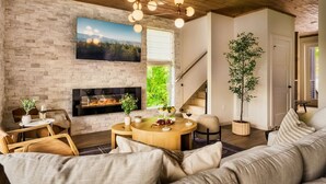 A cozy living room with a fireplace, a round wooden table, comfortable seating, and a staircase leading to another level. - POOL/Sauna/Hot Tub/VIEWS! - Half Moon Haven (Gatlinburg)