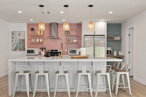 Una cocina moderna con una isla central, taburetes de bar, luces colgantes y un refrigerador.