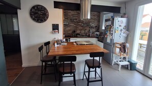 Una cocina moderna con una isla de madera, sillas negras, un extractor de acero inoxidable y un refrigerador con imanes.