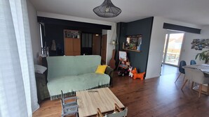 Una sala de estar con un sofá verde claro, mesa de comedor de madera y sillas. Hay un aparador de madera, una lámpara colgante y una pizarra con dibujos.