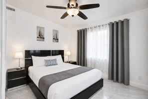 Ein modernes Hotelzimmer mit einem Bett, zwei Nachttischen, einem Deckenventilator und einem Fenster mit Vorhängen.