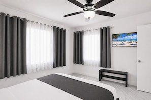 Une chambre à coucher avec un lit, un ventilateur de plafond et un tableau représentant une scène de plage.