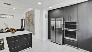 A modern kitchen with a large island, stainless steel appliances, and a world map on the wall.