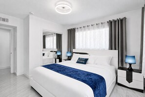 Habitación de hotel moderna con una cama grande, dos mesitas de noche con lámparas, un espejo y vistas al exterior.