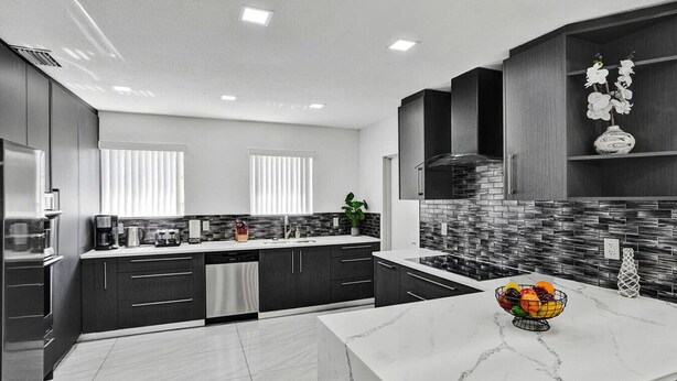 A modern kitchen with dark cabinetry, a marble countertop, and a backsplash with a mosaic tile design.