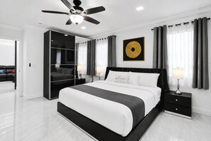 A modern bedroom with a large bed, a wardrobe, a ceiling fan, and a decorative wall piece.