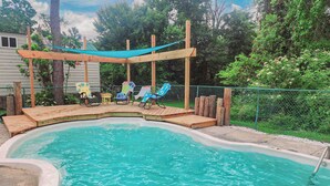 Ein Garten mit Pool, Holzterrasse und Sitzbereich mit Stühlen und Tisch.