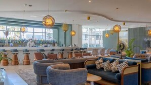 A modern bar area with high stools, a sofa, and hanging pendant lights. - New luxury resort on Medano Beach, (Cabo San Lucas)