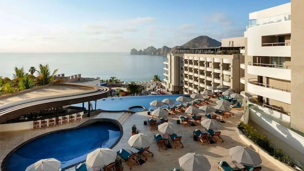 A resort with a large pool, sun loungers, and a view of the sea. - New luxury resort on Medano Beach, (Cabo San Lucas)