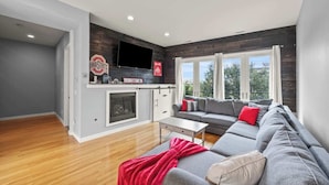 Un salon moderne avec un canapé gris, un plaid rouge et un t éléviseur à écran plat fixé au-dessus d’une cheminée.