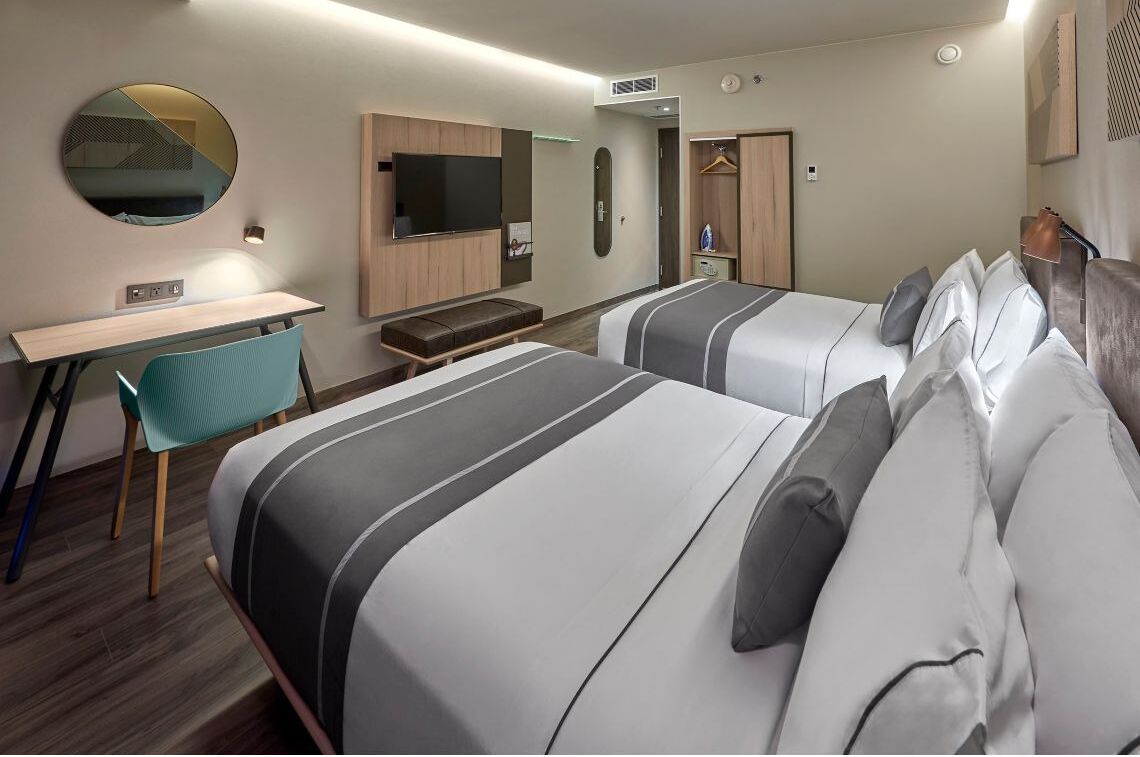 Habitació d'hotel amb dos llits, una taula de nit, una cadira, un televisor, un mirall i un armari.
