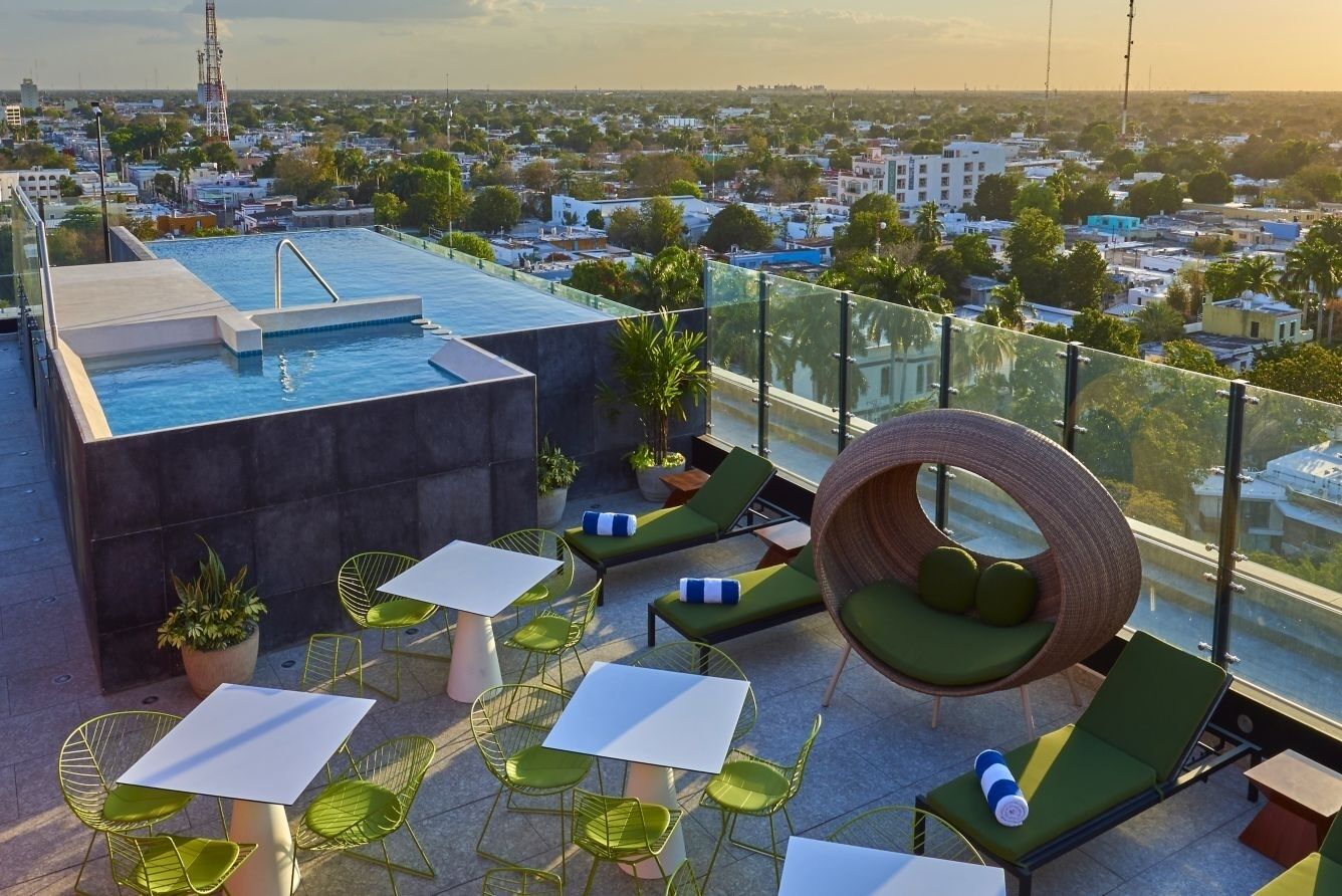 A rooftop terrace with a swimming pool, green lounge chairs, and tables.