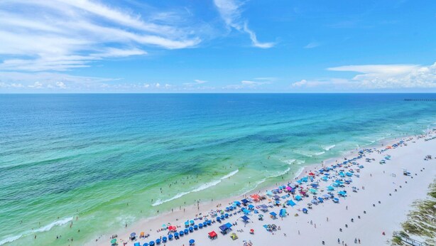 A beach with clear turquoise waters and a wide sandy area with numerous umbrellas and beachgoers. - Majestic Beach Towers 1-1909 (Panama City Beach)