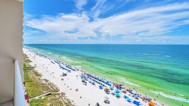 Ein Strand mit klarem türkisblauem Wasser, einem weiten Sandstrand und wolkenlosem Himmel.